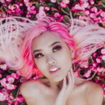 portrait_of_woman_with_pink_dyedhair and nose piercing lying on cluster of pink flowers - you don't want to coompost dyed hair