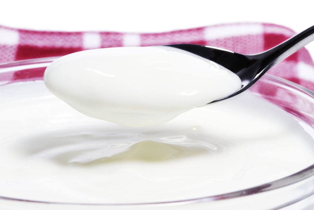 yogurt on a spoon over a yogurt dessert - can you compost yogurt?