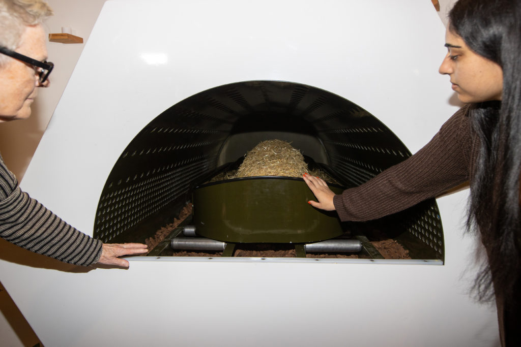 Two people look at a shrouded mannequin inside the Threshold Vessel in the Gathering Space at Recompose, a green funeral home specializing in human composting